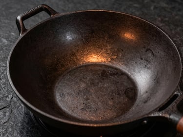 Close-up of a textured uncoated cast iron wok on a dark stone background, dramatic side lighting