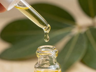 Macro detail shot of golden cold-pressed jojoba oil dripping into a clear glass vial, bright natural daylight, sharp focus on the droplet.