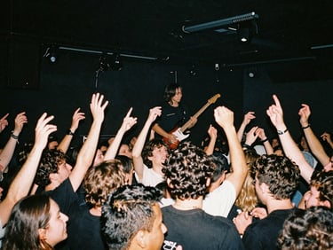 Candid wide-angle shot of a live band performing on stage, high-contrast concert lighting, energetic crowd, raw flash photography.