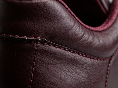 Extreme macro close-up of premium leather sneaker stitching, burgundy thread, dramatic high-contrast studio lighting