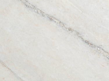 Macro shot of Pearl White granite slab surface under controlled studio raking light — creamy off-white ground with soft grey mineral streaks and faint silver mica flecks, honed finish showing subtle surface texture without high gloss