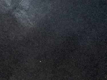 Close-up of Absolute Black granite slab under raking natural daylight — uniform dense black ground with zero visible grain variation, mirror-polished finish, sharp specular highlight running across the upper left of the surface