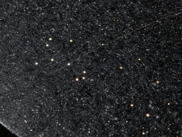 Extreme close-up of Galaxy Black granite slab surface under raking studio light — deep black ground with dense silver and gold mineral star-pattern inclusions, polished finish, light catching the metallic flecks at an oblique angle