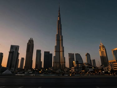 Cinematic wide-angle shot of the Dubai skyline at golden hour, dramatic twilight shadows stretching across iconic skyscrapers, warm ambient glows.