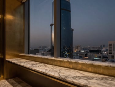Moody architectural detail of a private office in Latifa Tower, Sheikh Zayed Road, with marble surfaces, warm brass accents, and twilight city views through the window.