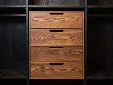 Straight-on architectural elevation of a bespoke black oak closet system, warm directional light highlighting grain-matched timber drawers and integrated shelving