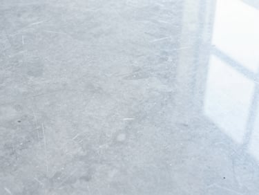 Close-up shot of a heavily scuffed and dull grey marble floor, visible scratches and water stains under soft overhead light
