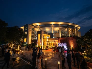 Wide-angle prestigious editorial photography of Talkatora Stadium exterior under dramatic golden evening lights, New Delhi, deep navy sky, professional hospitality event atmosphere