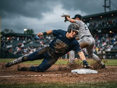 Low-angle action shot of a baseball player sliding into second base, dirt flying, high contrast dramatic overcast light, 35mm