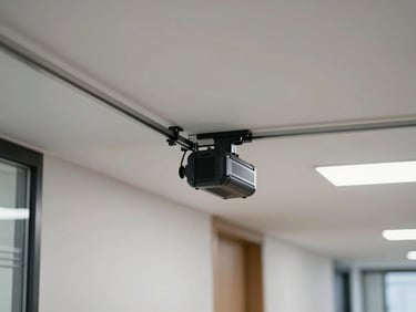 Motorized curtain track and motor unit mounted to a commercial ceiling track in an office corridor, bright even ambient light, medium-distance straight-on angle showing the motor housing and rail clearly