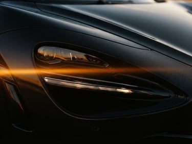 Extreme close-up of a sleek black supercar headlight, golden hour rim light reflecting off carbon fiber, anamorphic lens flare, 35mm cinematic film photography