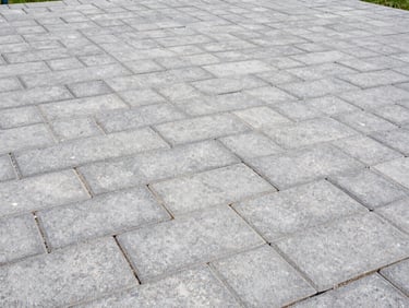 Wide shot of a newly installed grey block paving patio with crisp edges, bright overcast daylight, natural colors with sharp contrast, 35mm