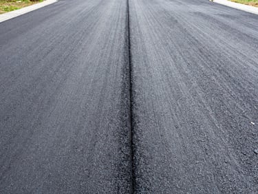 Detail shot of a new asphalt driveway with a visible drainage channel, bright overcast daylight, natural colors with sharp contrast, 35mm