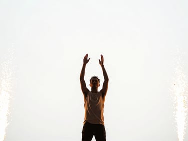Wide-angle dynamic shot of an artist performing on a bright stage flooded with warm golden flares, hands raised, high-contrast clean white backdrop, brilliant lighting, 35mm lens