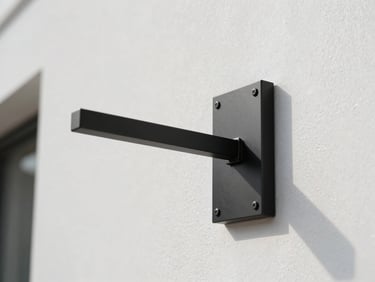 Wall sconce bracket in matte black steel mounted flush against a smooth white plaster wall, architectural daylight from upper left, extreme lateral framing showing the arm's sectional profile and weld integrity, no decor