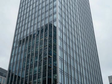 Wide architectural perspective of a modern glass-and-steel skyscraper facade in a global financial district, cool overcast daylight, desaturated blue and slate tones, sharp focus