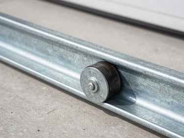 Close-up of heavy-duty steel garage door rollers seated in a galvanized track, high-contrast metallic tones.