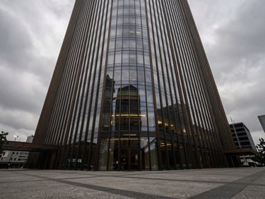 Extreme wide-angle shot of a modern glass office tower reflecting an overcast grey sky, monumental concrete plaza below