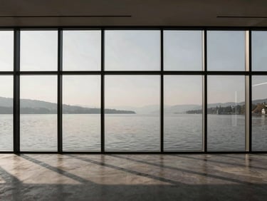 Minimalist interior of an architecture office in Geneva, soaring glass windows overlooking a serene grey lake, sharp geometric shadows