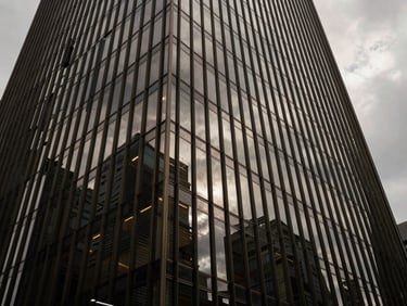 Wide-angle architectural shot of a modern glass skyscraper facade reflecting dramatic overcast skies, sharp shadows, minimalist steel lines, premium architectural photography