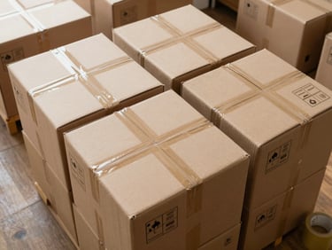 Wide overhead view of packed cardboard boxes labeled by room and fragility level, neatly stacked and organized on a wooden floor with packing tape rolls visible at the edge, natural daylight from above
