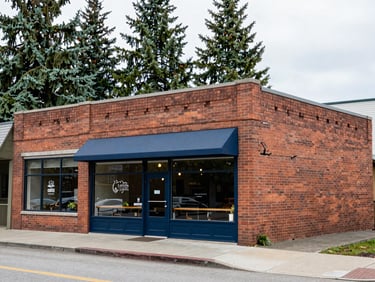 A historic brick building housing a local coffee shop in Spokane, soft natural daylight, clean sidewalk, evergreen trees in background.