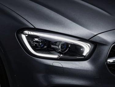 Macro shot of a modern luxury car headlight, high-contrast studio strobes, deep charcoal metallic paint