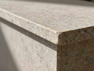 Close-up of a stone fabrication edge detail — a precisely routed travertine countertop profile photographed from side elevation in north-facing studio light, showing tool marks and material texture