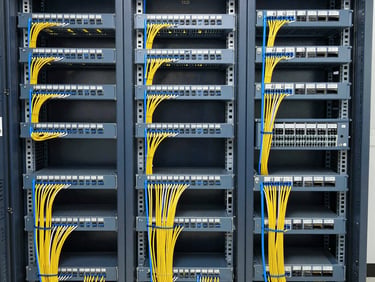 Wide environmental shot of a structured enterprise network closet, patch panels fully populated with colour-coded cables running in neat horizontal trays, rack-mounted switches with organised cable bundles, bright even overhead lighting showing clean termination standards and labelling throughout, framed to capture full rack height and cable pathway