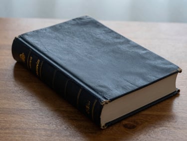 Close-up under warm desk light of a vintage leather-bound book on a wooden desk, title gold-embossed on the spine