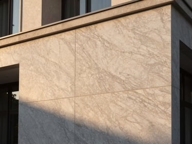 Wide close-up of marble-textured exterior cladding on a residential building facade in golden hour light, veining patterns catching warm directional sun, stone grain depth visible in the surface shadows