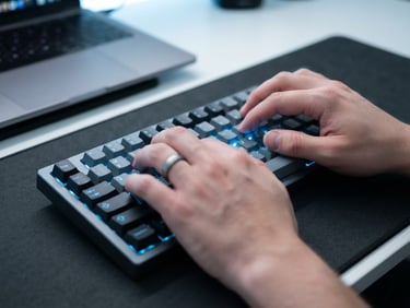 Close-up of hands typing on a modern mechanical keyboard, glowing cool blue backlighting, sharp focus, minimalist tech photography style