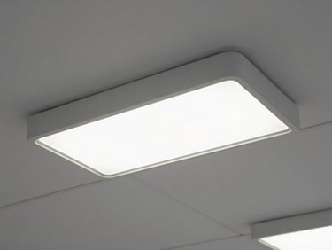 Overhead detail shot of recessed LED luminaire fixtures installed in a suspended ceiling grid inside a finished commercial space, even diffuse lighting, no people, clean white ceiling tiles