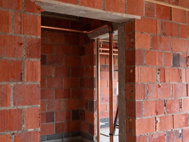 Interior construction site, exposed brick walls, copper pipes visible, high contrast red tones