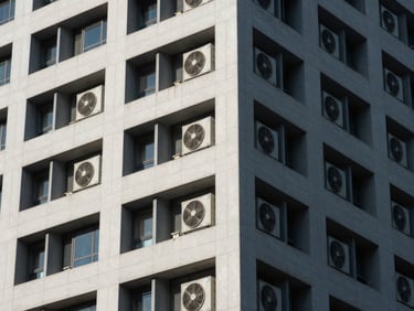 Clean architectural lines of a commercial high-rise exterior, showing industrial HVAC installations under sharp architectural shadows.