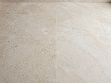 Split-frame of a travertine floor — left side shows dull, mineral-stained surface with white calcium deposits visible in the pores, right side shows the same stone restored to a clean polished finish, consistent bathroom overhead light, no styling
