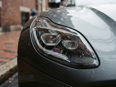 Close-up of a modern luxury vehicle headlight reflecting historic Boston brick architecture on Charles Street, overcast daylight, 35mm photography