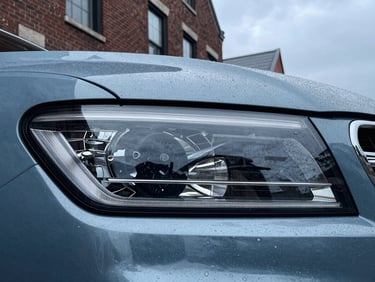 Tight editorial crop of a modern vehicle headlight reflecting historic brick architecture on Charles Street, crisp overcast daylight, cool blue tones.