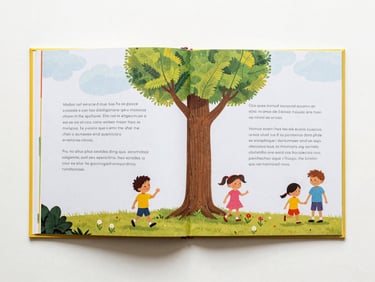Overhead flat-lay of a bilingual children's book open to a two-page spread, English text on the left page and Spanish on the right, both pages showing the same illustration integrated into the layout, clean studio lighting on a white surface