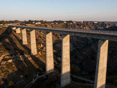 Extreme wide technical aerial perspective of a massive concrete bridge spanning a deep valley, golden hour light casting long dramatic shadows, sharp cinematic details, 35mm