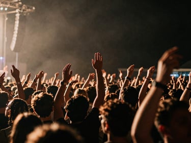 Dynamic wide-angle shot of a music festival crowd, hands in the air, dramatic stage lighting, high-contrast, deep shadows, rich warm tones, 35mm film grain.
