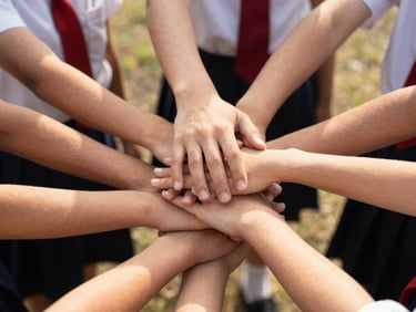 Hands of school community members stacked together in solidarity, warm natural light, authentic connection.