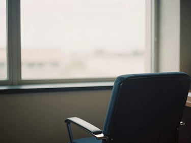A quiet corner of a professional office, a comfortable chair facing a large window, diffused natural light, a sense of calm and contemplation, warm editorial photography.
