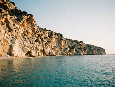 Wide-angle panoramic shot of a quiet turquoise cove in Greece, golden hour sun hitting the limestone cliffs, no people, 35mm film grain style
