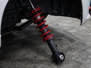 Close-up of a car's suspension system, including a shock absorber and control arm, on a concrete floor, dramatic low-key lighting, industrial automotive photography.