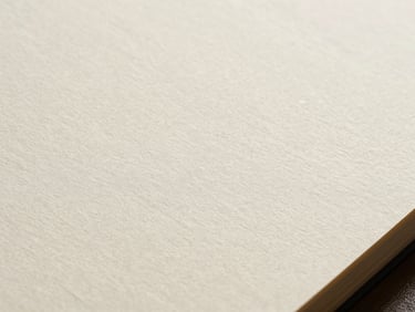 Extreme close-up of offset paper surface, smooth uncoated texture visible under diffuse daylight, cream-white tone, paper grain detail prominent, single sheet held slightly angled
