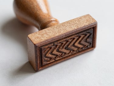 Macro photograph of a laser-engraved wooden hand stamp resting on a clean sheet of paper, soft side-light showing the sharp rubber details