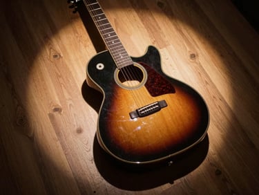 Tight overhead shot of a guitar body resting on a wooden studio floor, a single warm spotlight from above creating a circular halo, deep shadow at the edges — no people, no text