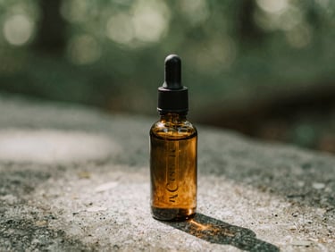 A small amber glass dropper bottle resting on a textured stone surface, soft dappled forest light