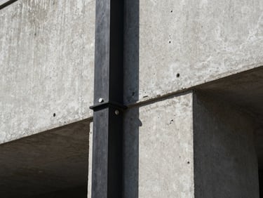 Detailed close-up of structural raw concrete meeting a perfectly aligned black steel column, sharp daylight, technical architectural detail.
